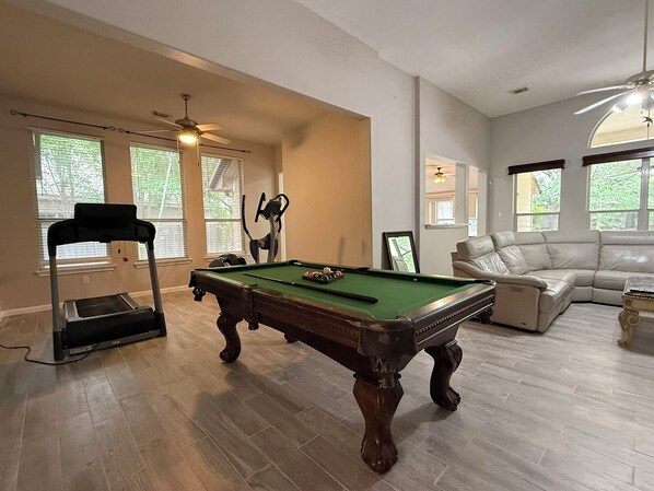 A spacious living room with a pool table, a treadmill, and a leather sofa. - Bright and Spacious 6BR Amber Crest Home with Pool Table and Gated Entry (San Antonio)