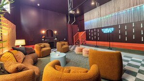 A modern lobby with a checkered floor, plush seating, a staircase, and a neon sign.