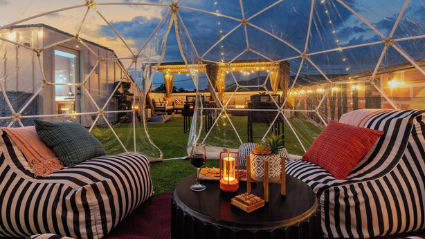 A geodesic dome structure with a seating area featuring striped sofas and a table with a wine glass, candle, and snacks.