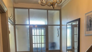 A hallway with a wooden floor, a glass door with frosted glass panels, a chandelier, and a staircase with white balusters.