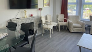 A living room with a stone fireplace, a flat-screen TV, and a dining area with a glass table and chairs.
