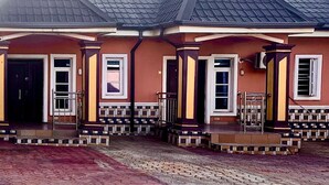 A two-story house with a dark roof, a front porch with steps, and a brick driveway. - MC RICA HOTEL (Ikorodu)