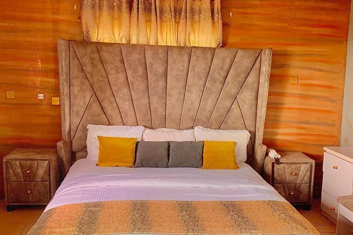 A bedroom with a large bed, wooden panel walls, a tufted headboard, and a nightstand with a lamp.