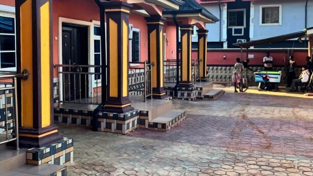 A building with a tiled roof and a red and yellow facade. - MC RICA HOTEL (Ikorodu)