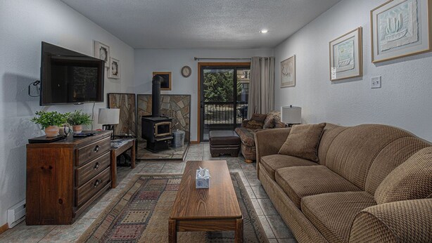 A cozy living room with a fireplace, a sofa, a coffee table, and a television. - Budget-Friendly Purgatory Condo, Steps to Lift, Hot Tub, w/ Pool & Gym Access (Durango)
