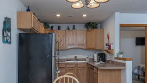 A compact kitchen with wooden cabinets, a black refrigerator, a dining table with chairs, and a small countertop with a coffee maker. - Budget-Friendly Purgatory Condo, Steps to Lift, Hot Tub, w/ Pool & Gym Access (Durango)
