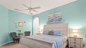 A bedroom with a wooden bed, two bedside tables, a ceiling fan, and artwork on the wall. - Poolside At Calabay - Home for 11 With Game Room, Pool & Hot Tub (Davenport)