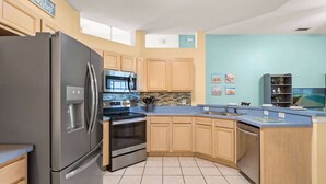 A kitchen with a stainless steel refrigerator, double oven, and microwave. There are wooden cabinets and a blue countertop. - Poolside At Calabay - Home for 11 With Game Room, Pool & Hot Tub (Davenport)