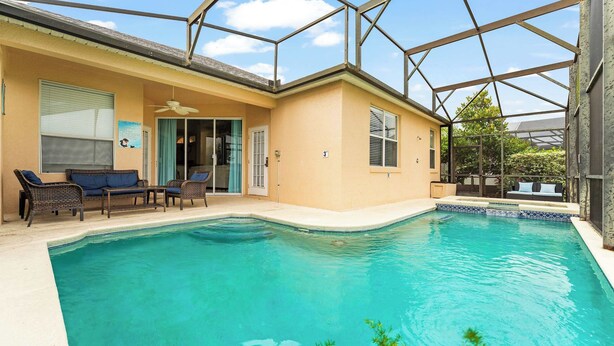A swimming pool with a glass enclosure, a patio with wicker furniture, and a door leading to a covered area. - Poolside At Calabay - Home for 11 With Game Room, Pool & Hot Tub (Davenport)