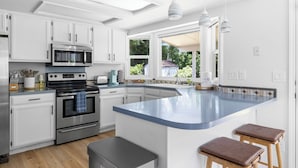 A modern kitchen with white cabinetry, stainless steel appliances, a large island with stools, and a view of greenery outside. - Perfect for Families & Pets, Garage Parking, Stylish Renovation, Sleeps 10 (Boise)
