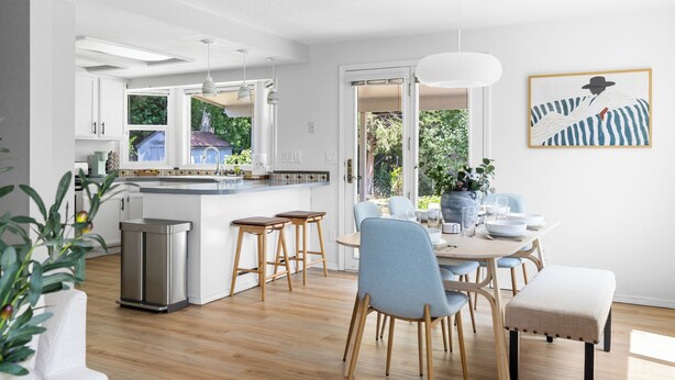 A modern kitchen with white cabinetry, a central island, and pendant lighting. There is a dining area with a round table and blue chairs. - Perfect for Families & Pets, Garage Parking, Stylish Renovation, Sleeps 10 (Boise)