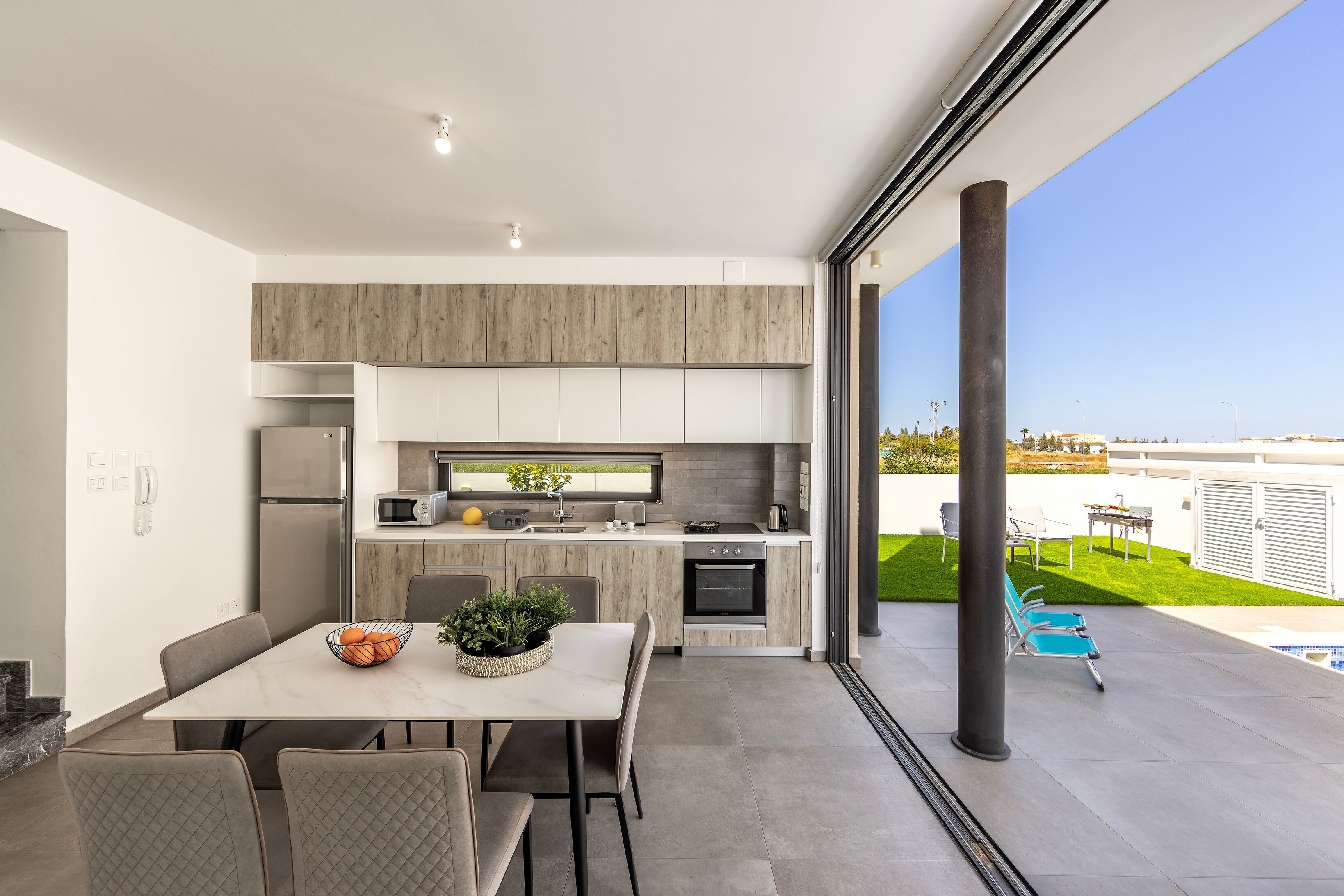 A modern kitchen with a dining area, large windows, and a view of a pool and garden.