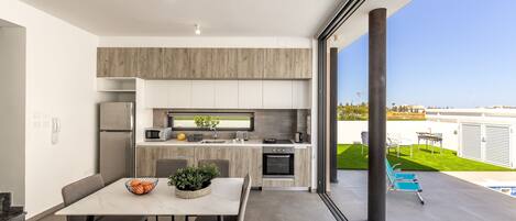A modern kitchen with a dining area, large windows, and a view of a pool and garden.