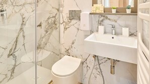 Une salle de bain moderne avec une douche à parois de verre, un lavabo blanc et un mur décoré d’un motif marbré.