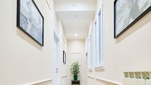 Un couloir avec des tableaux encadrés accrochés aux murs, une plante en pot et un radiateur.