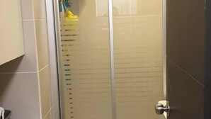 A small, enclosed shower area with a glass door, a washing machine, and a dark mat on the floor. - Spring Residences by VnB (Paranaque)