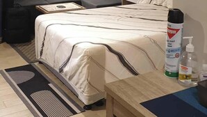A bedroom with a bed, bedside table, and a desk. There is a ceiling fan, an air conditioning unit, and a window with blinds. - Spring Residences by VnB (Paranaque)