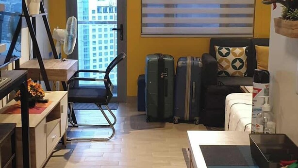 A compact living space with a kitchenette, a dining area, and a seating area with a view of the cityscape through large windows. - Spring Residences by VnB (Paranaque)