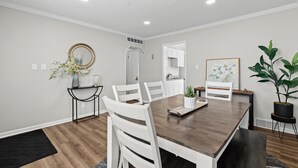 Un coin repas avec une table en bois, des chaises blanches, un vase de fleurs et une plante en pot.