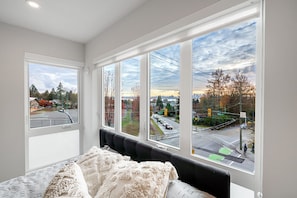 Een slaapkamer met een groot raam met uitzicht op een stadstraat en een verkeerslicht.