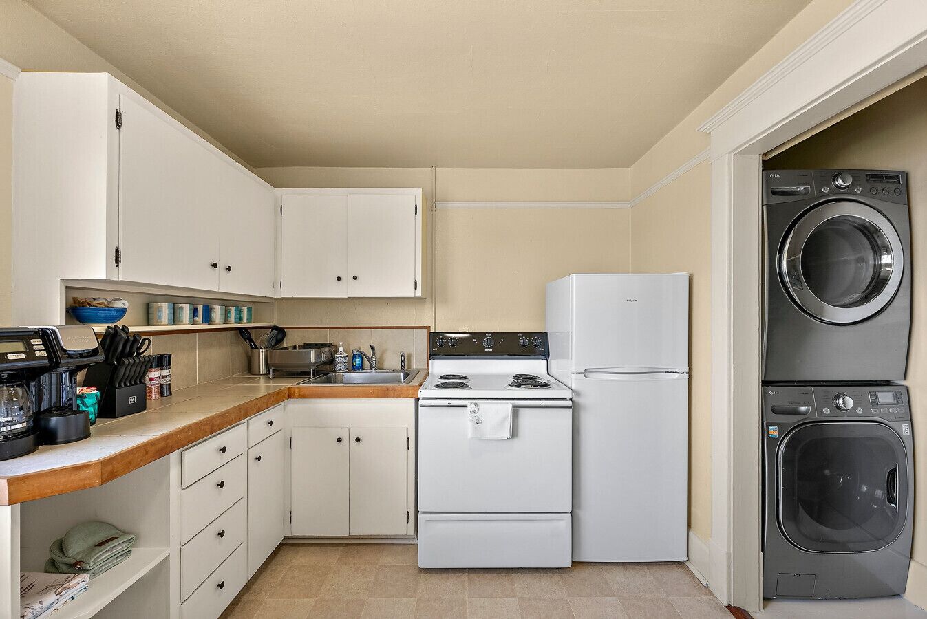 A compact kitchen with white cabinets, a stove, a refrigerator, and a stacked washer and dryer.