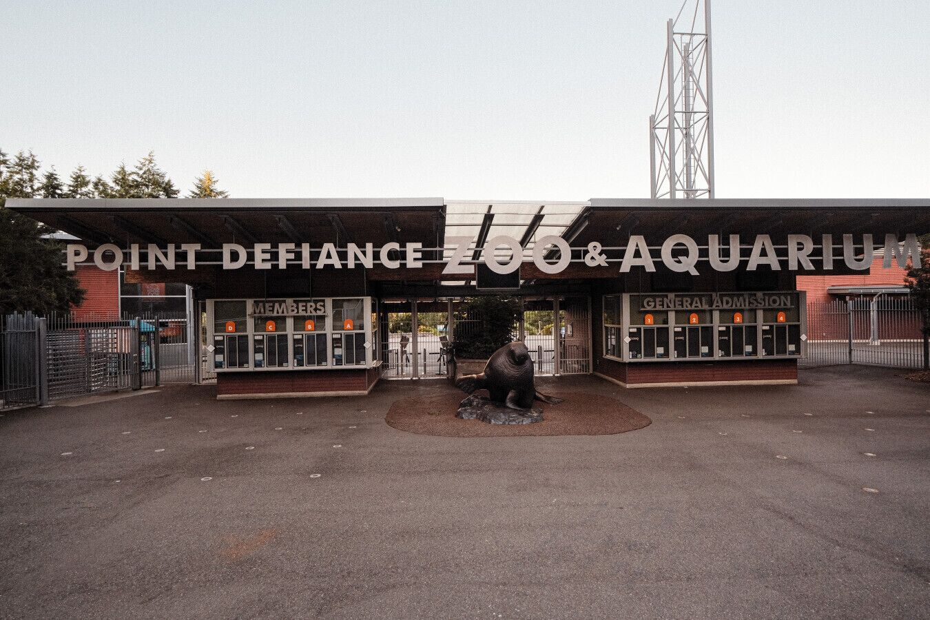 De ingang van Point Defiance Zoo & Aquarium, met een groot bord, een kaartjeshok en een standbeeld van een zeehond.
