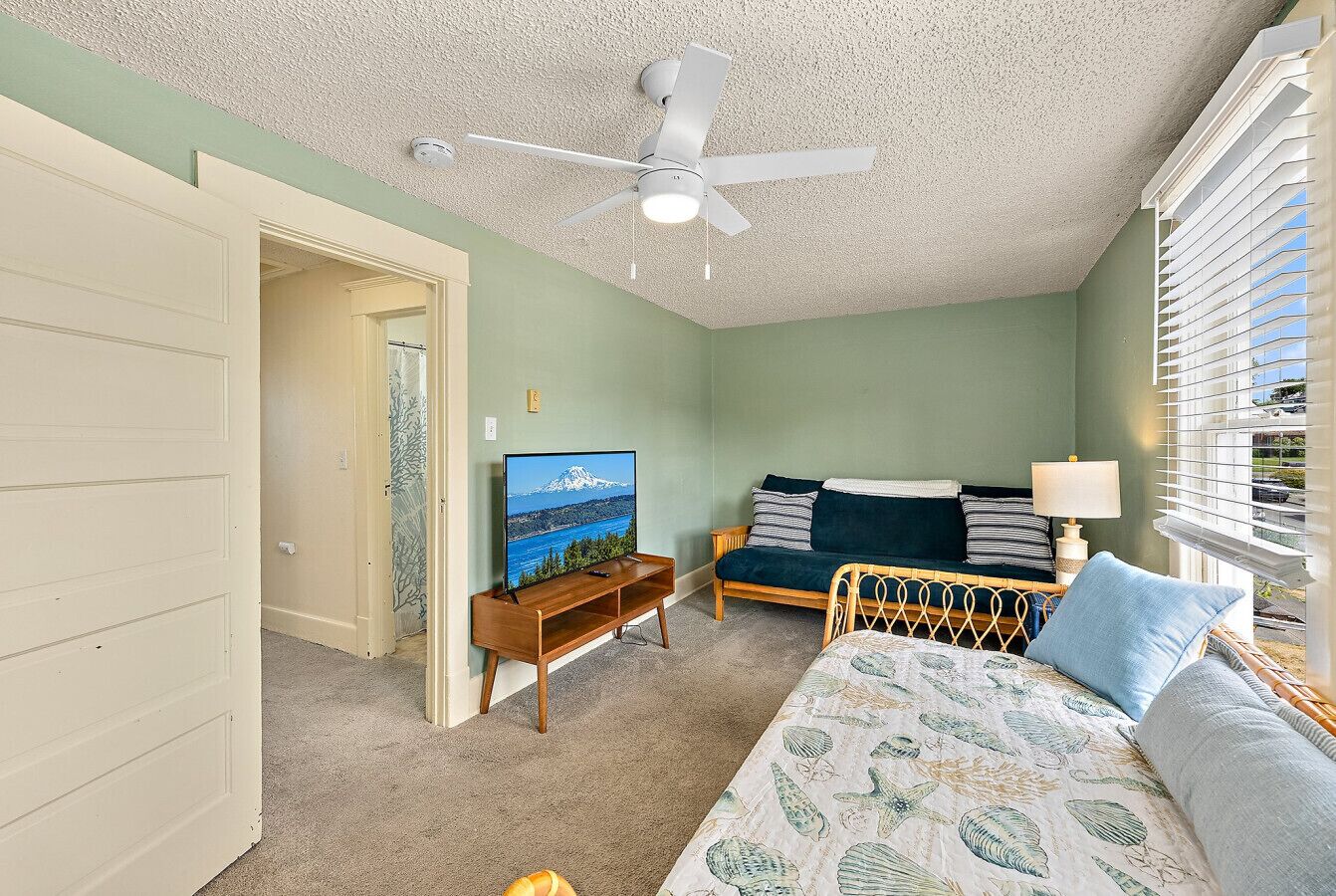 A bedroom with a bed, a TV, a ceiling fan, and a window with blinds.