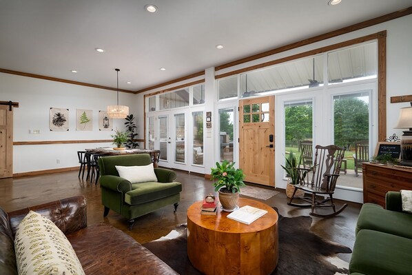 A spacious living room with a large window, a wooden coffee table, and a green armchair.