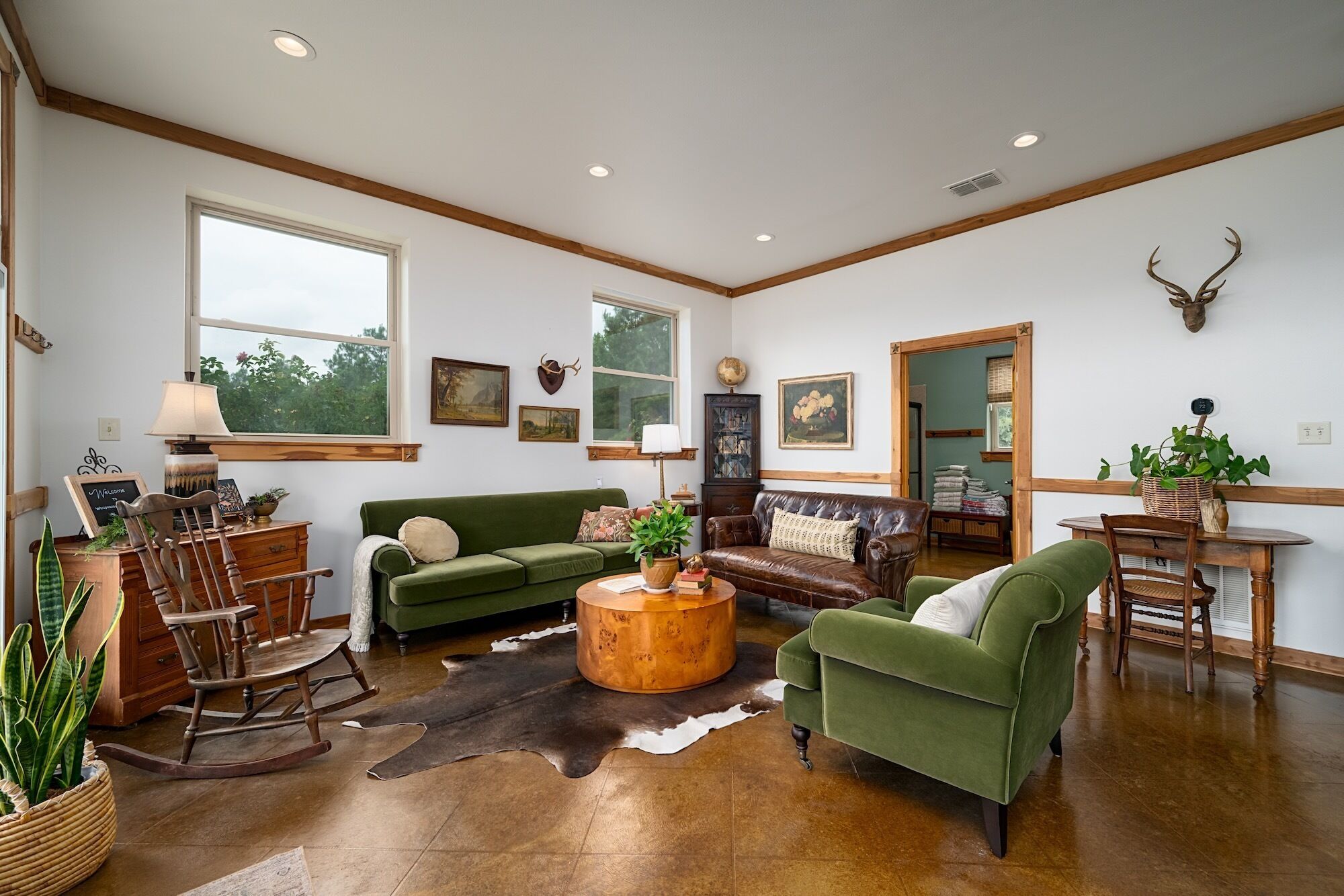 A spacious living room with a green sofa, a leather couch, a wooden rocking chair, a coffee table, and a cowhide rug.
