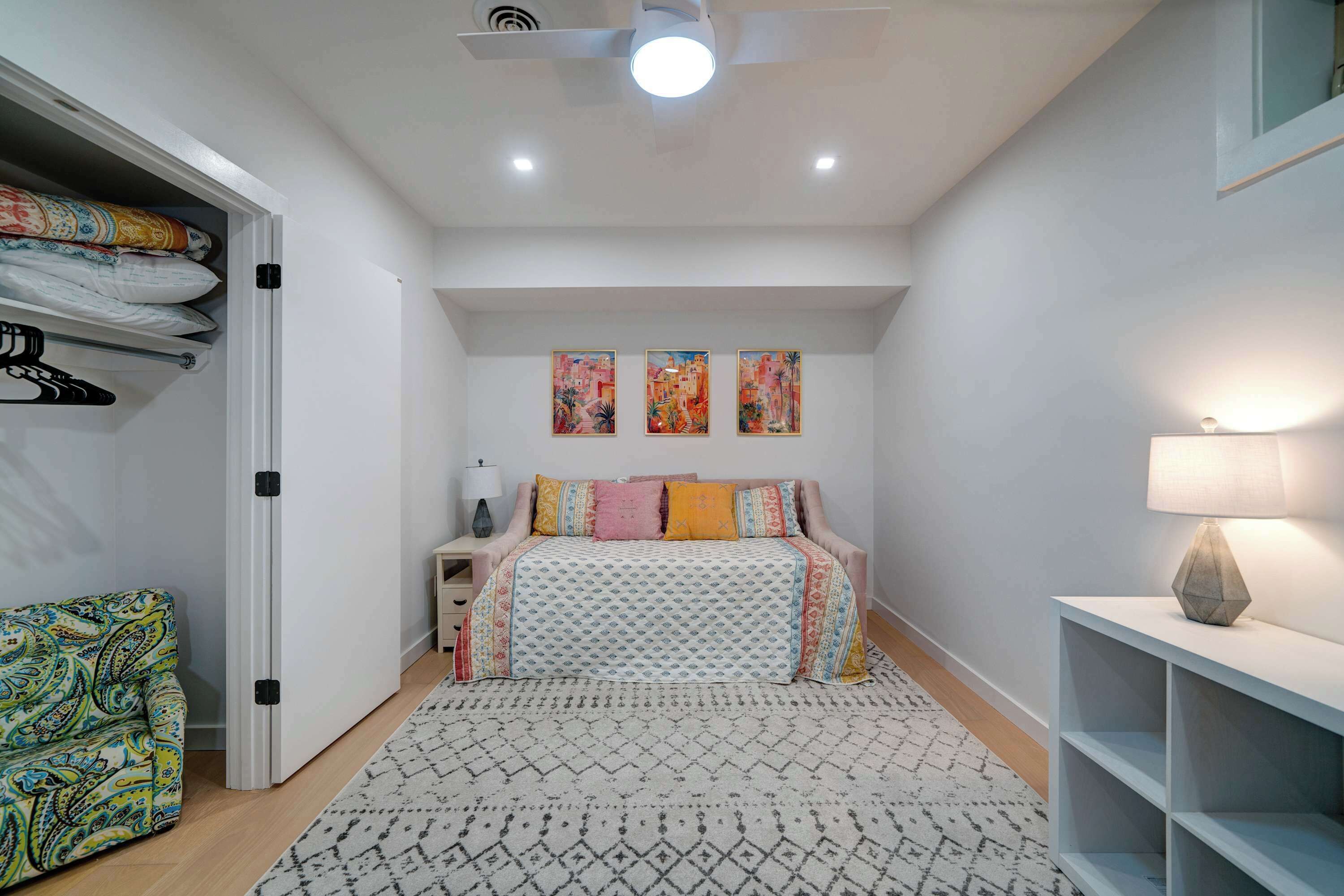 Ein Schlafzimmer mit Bett, Nachttisch, Lampe, Kleiderschrank und einem gemusterten Teppich.