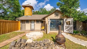 Une maison avec une façade en bois, un puits en pierre et un foyer extérieur en métal.