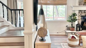 Amplia sala de estar con una escalera de madera, un televisor de pantalla plana montado en la pared, una lámpara de mimbre sobre una consola de madera y una chimenea de piedra.