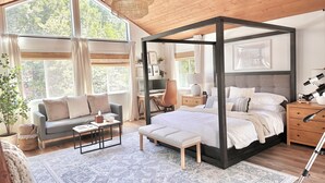 Un dormitorio con cama con dosel, un escritorio con computadora, un sofá y un amplio ventanal con cortinas.