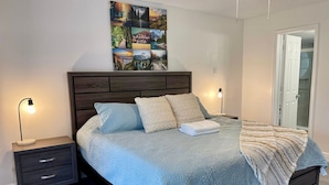A bedroom with a bed, two bedside tables, a nightstand, a wall art piece, and a door.