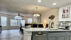 A spacious kitchen with a central island, modern appliances, and a view of the outside through large windows.