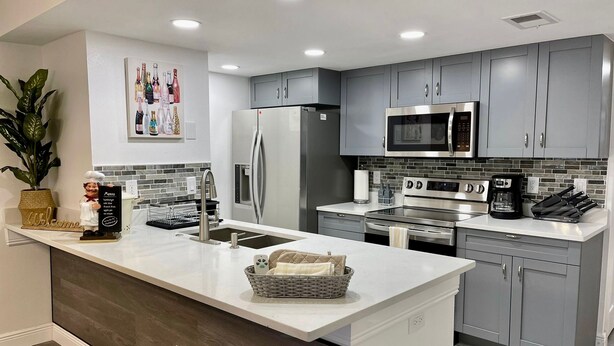A modern kitchen with grey cabinets, stainless steel appliances, and a central island.