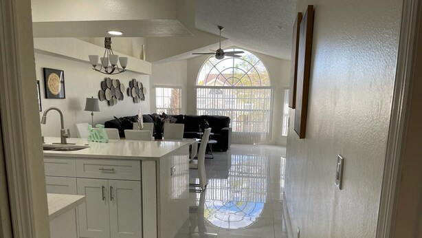 Een moderne keuken met een centraal eiland, witte kasten en een eethoek met een zwarte bank.