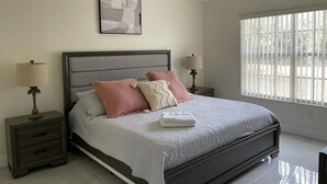 Een slaapkamer met een bed, nachtkastjes, een plafondventilator, een raam met jaloezieën en een ingelijste foto aan de muur.