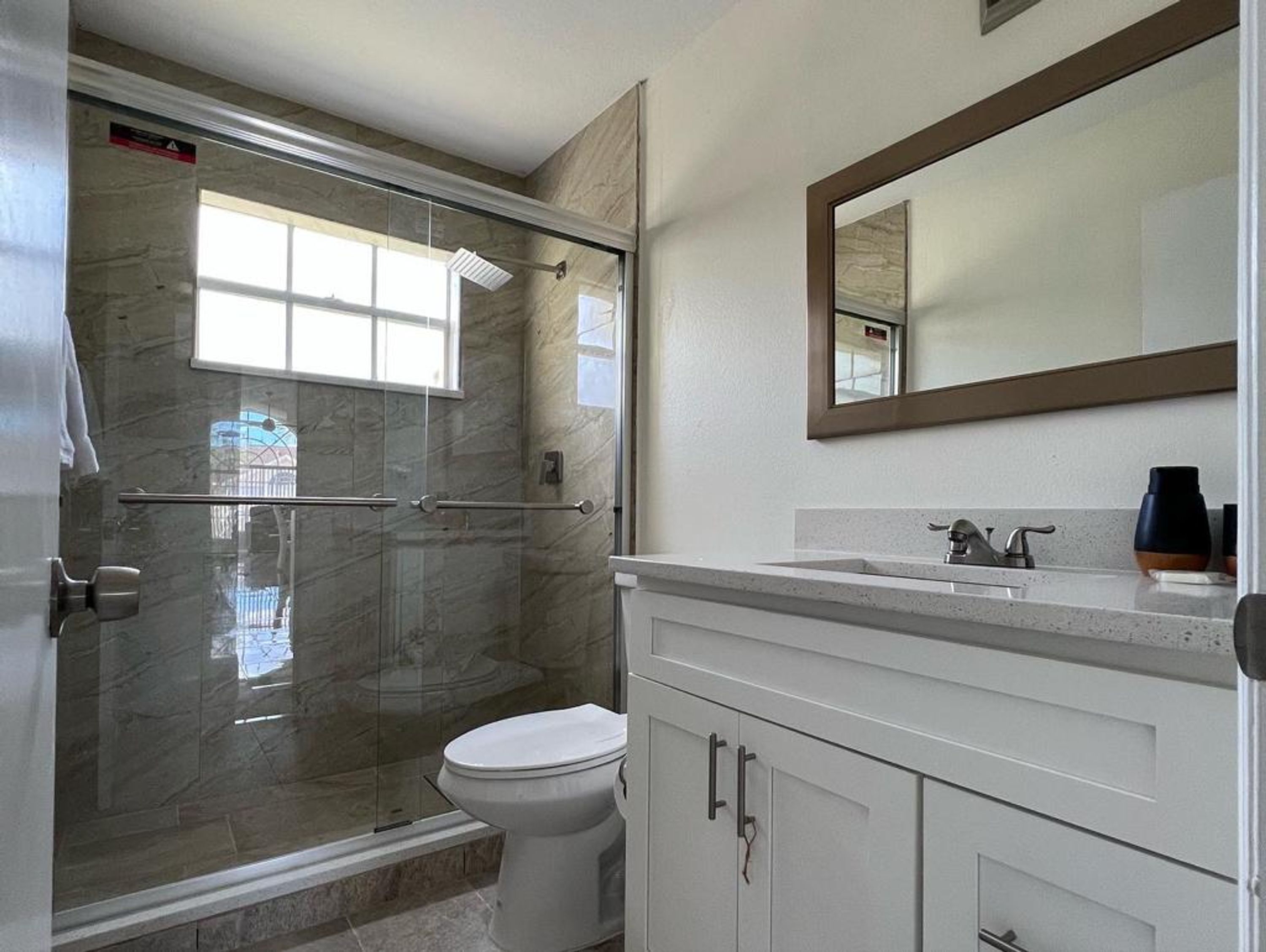 A bathroom with a glass-enclosed shower, a toilet, and a vanity with a mirror.