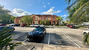 A parking lot with multiple cars and a building with a red roof in the background. - Luxury Compass 3BR Townhouse Near Disney Parks 2 (Kissimmee)