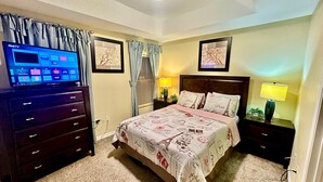A bedroom with a bed, a TV on a dresser, a nightstand with a lamp, and two framed pictures on the wall. - Luxury Compass 3BR Townhouse Near Disney Parks 2 (Kissimmee)