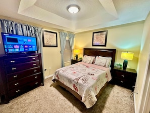 A bedroom with a bed, a TV on a dresser, a nightstand with a lamp, and two framed pictures on the wall. - Luxury Compass 3BR Townhouse Near Disney Parks 2 (Kissimmee)