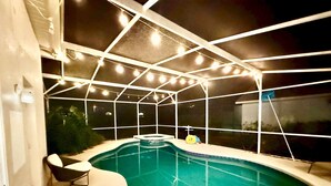 A swimming pool with a covered area, surrounded by a white frame structure, and a small seating area with a chair and a stool. - Westridge Super Exclusive 4BR Home Near Disney (Davenport)