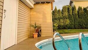 Una piscina con una escalera de metal, una valla de madera y una pequeña planta de palmera.