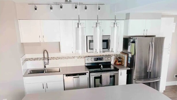 Una cocina moderna con armarios blancos, electrodomésticos de acero inoxidable y una isla central con taburetes.