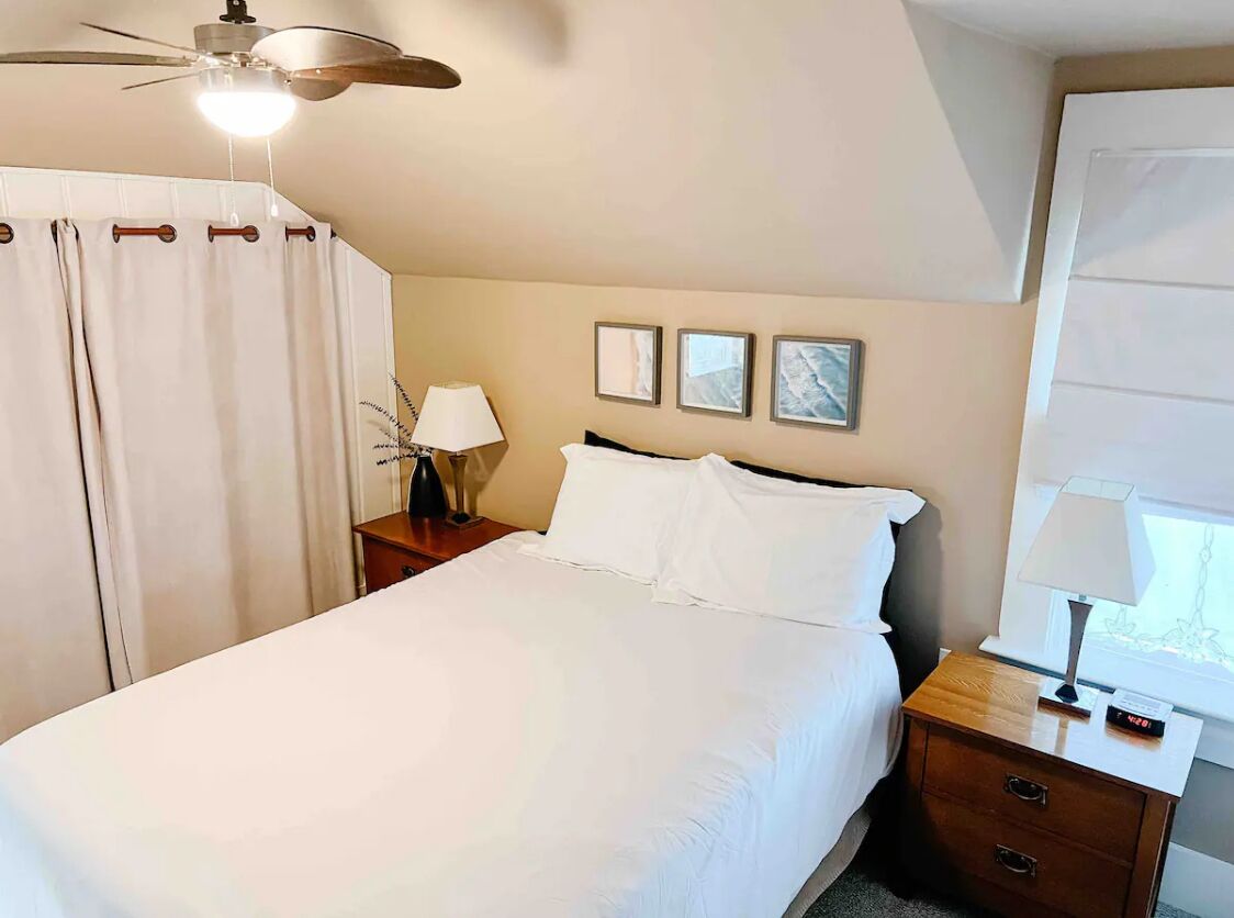 A hotel room with a bed, a nightstand, a lamp, a clock, and a ceiling fan.