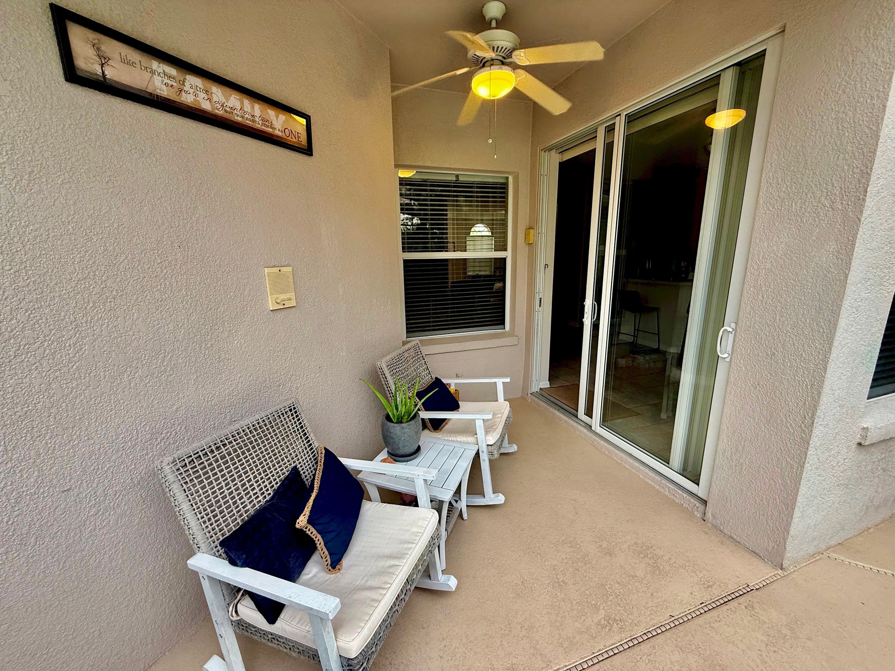 A covered patio with wicker furniture, a ceiling fan, and a sliding glass door leading to an interior space.
