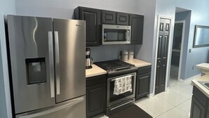 Une cuisine moderne dotée d’appareils électroménagers en acier inoxydable, de meubles de rangement aux couleurs sombres et d’un sol carrelé.