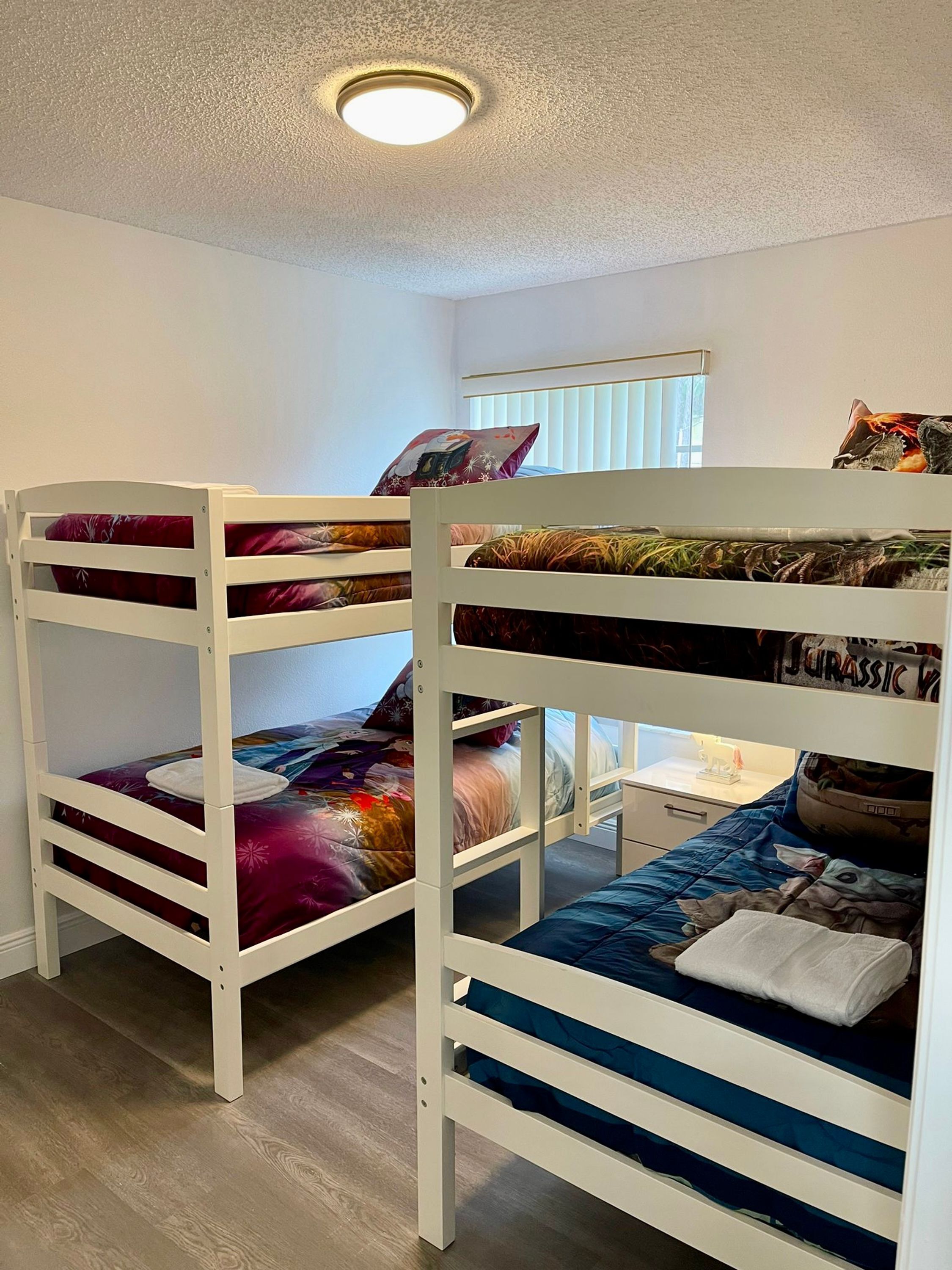 A bunk bed room with a window, a ceiling light, and a small table with a lamp.