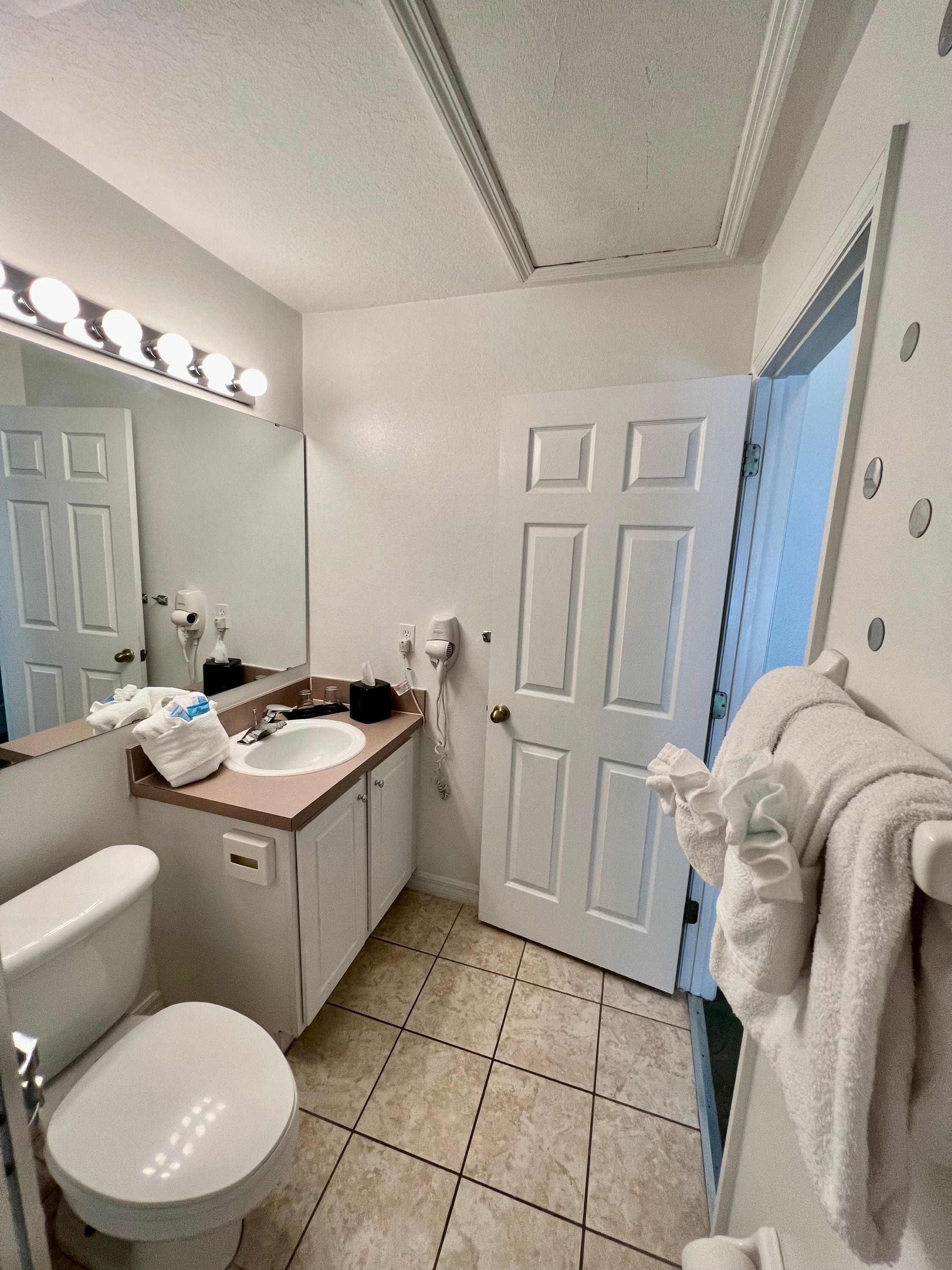 A bathroom with a white toilet, a sink, a mirror with lights, and a towel rack.